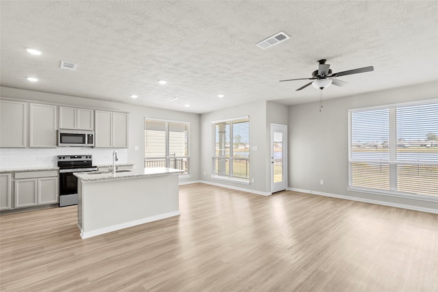 kitchen featuring light stone counters, a center island with sink, light hardwood / wood-style flooring, and appliances with stainless steel finishes