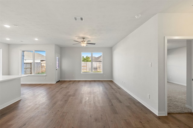 unfurnished living room with a wealth of natural light, visible vents, baseboards, and wood finished floors