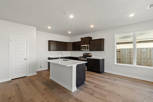 kitchen with recessed lighting, a sink, light countertops, appliances with stainless steel finishes, and light wood finished floors