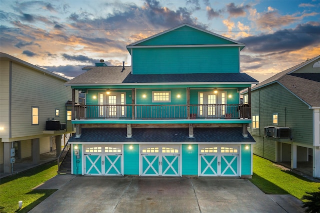 back house at dusk featuring a balcony, central AC unit, and a garage