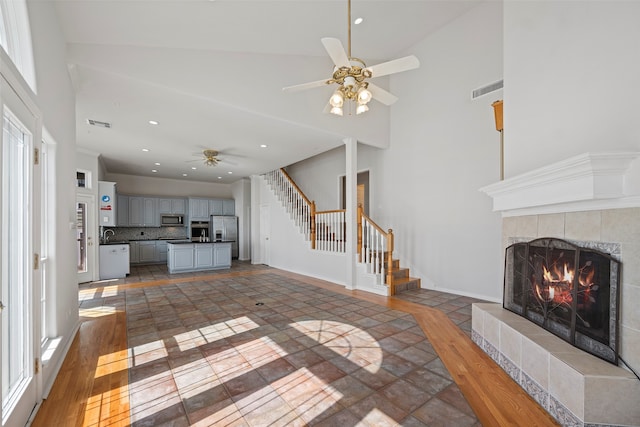 unfurnished living room featuring ceiling fan, a tiled fireplace, high vaulted ceiling, and hardwood / wood-style floors