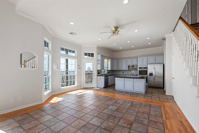 kitchen with gray cabinetry, tasteful backsplash, appliances with stainless steel finishes, a kitchen island, and crown molding