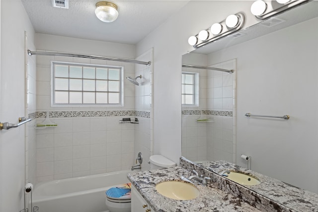 full bathroom featuring vanity, tiled shower / bath combo, a textured ceiling, and toilet