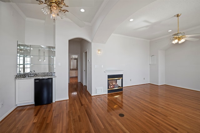 unfurnished living room featuring a multi sided fireplace, dark wood-type flooring, crown molding, and ceiling fan