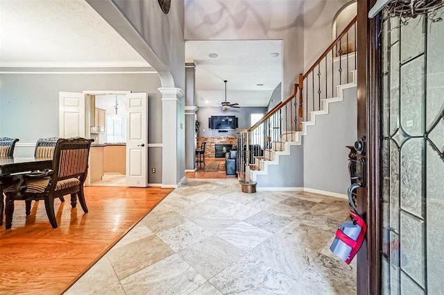 entryway featuring ceiling fan, ornamental molding, a fireplace, wood-type flooring, and decorative columns