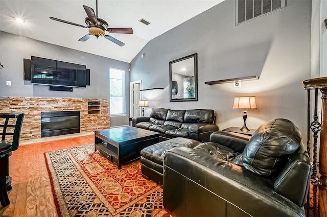 living room with hardwood / wood-style flooring, ceiling fan, a stone fireplace, and lofted ceiling