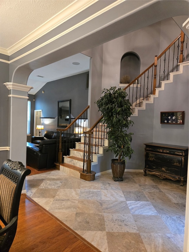 foyer entrance with a textured ceiling, ornate columns, and crown molding