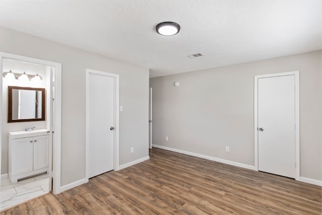 unfurnished bedroom with connected bathroom, hardwood / wood-style floors, a textured ceiling, and sink