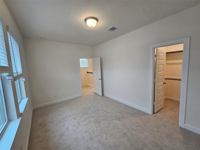 unfurnished bedroom featuring a walk in closet, a closet, light colored carpet, and multiple windows