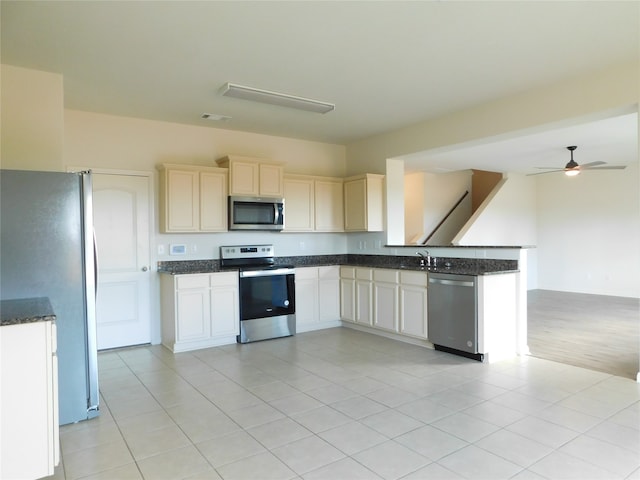 kitchen featuring appliances with stainless steel finishes, sink, light tile patterned flooring, ceiling fan, and dark stone counters