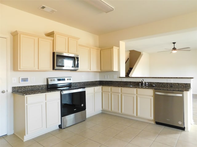 kitchen with stainless steel appliances, dark stone countertops, sink, light tile patterned floors, and ceiling fan