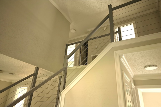 staircase with crown molding, a textured ceiling, and a healthy amount of sunlight