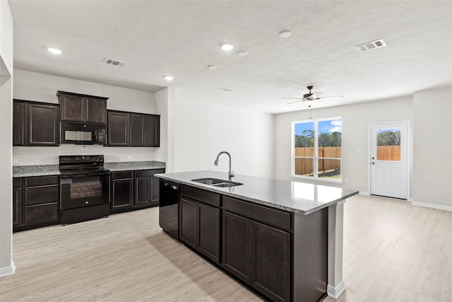 kitchen featuring black appliances, light hardwood / wood-style floors, sink, and a center island with sink