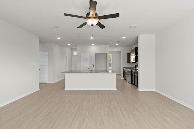 kitchen featuring light stone counters, appliances with stainless steel finishes, light hardwood / wood-style floors, ceiling fan, and a kitchen island with sink