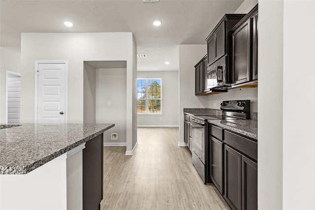 kitchen featuring stainless steel appliances, dark stone countertops, a textured ceiling, and light wood-type flooring