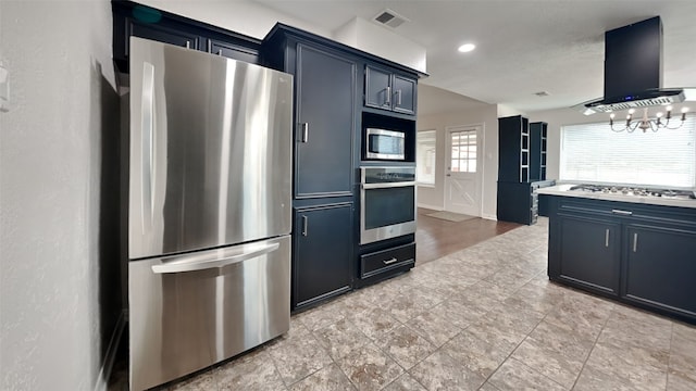 kitchen with blue cabinets, a notable chandelier, wall chimney range hood, and stainless steel appliances