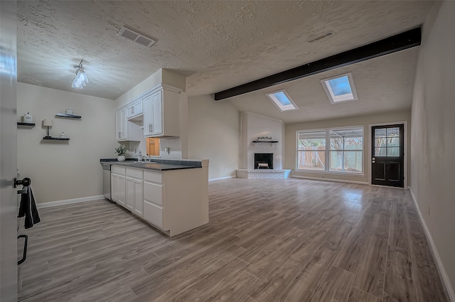 kitchen with sink, vaulted ceiling with skylight, light wood-type flooring, white cabinetry, and a fireplace