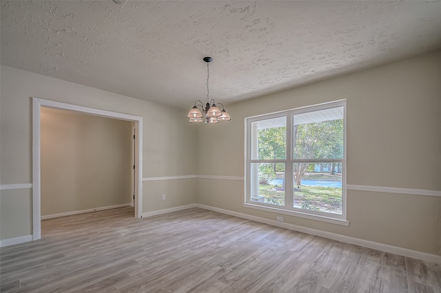 spare room with a chandelier, light hardwood / wood-style flooring, and a textured ceiling