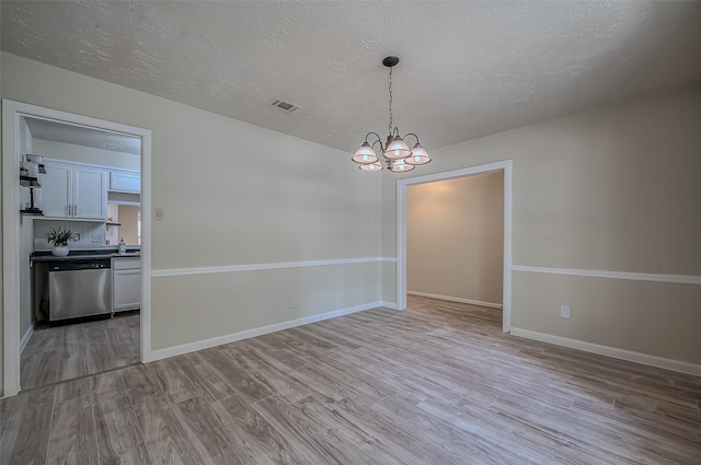 unfurnished dining area with a notable chandelier, a textured ceiling, and light hardwood / wood-style floors