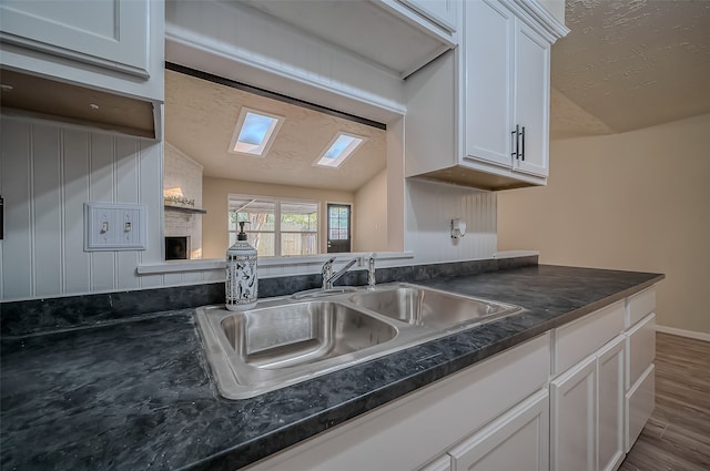 kitchen with hardwood / wood-style floors, sink, white cabinets, a fireplace, and a skylight