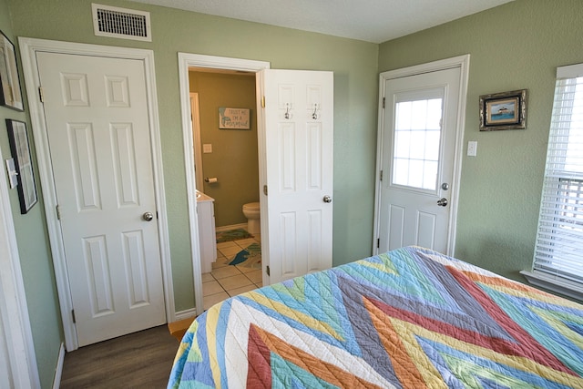 bedroom with ensuite bath, a textured ceiling, multiple windows, and dark hardwood / wood-style flooring