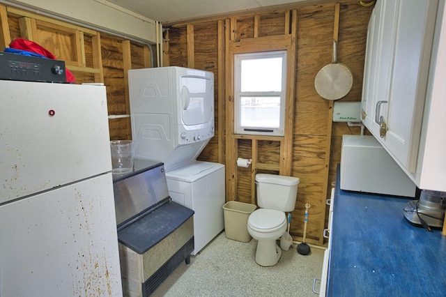bathroom featuring stacked washer / dryer and toilet