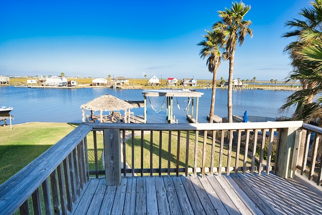 wooden terrace featuring a water view, a boat dock, and a lawn