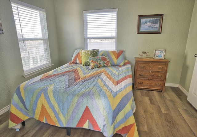bedroom with wood finished floors, baseboards, and multiple windows