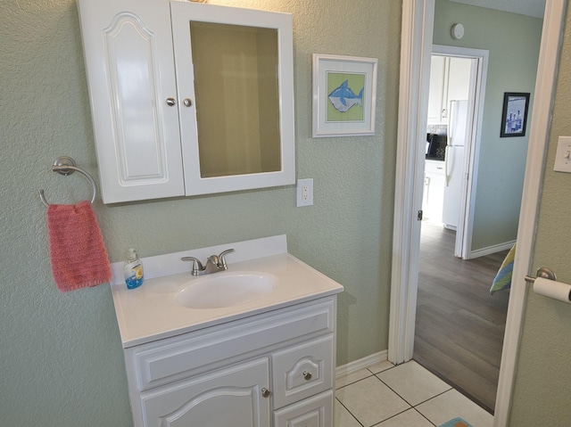 bathroom with tile patterned floors, baseboards, a textured wall, and vanity
