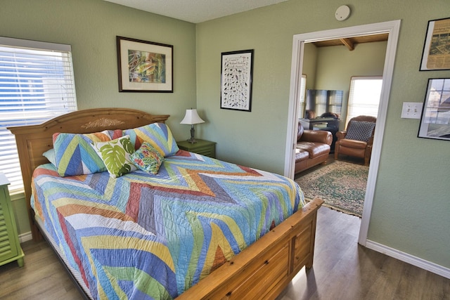 bedroom with wood finished floors, baseboards, and multiple windows