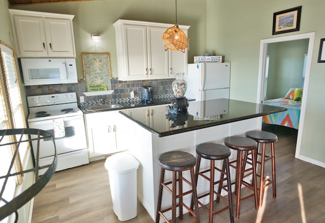 kitchen featuring a breakfast bar area, white cabinetry, light hardwood / wood-style floors, a center island, and white appliances