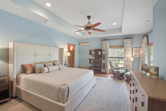 bedroom featuring an AC wall unit, light hardwood / wood-style flooring, ceiling fan, and a raised ceiling