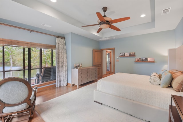 bedroom featuring ceiling fan, a tray ceiling, and wood-type flooring