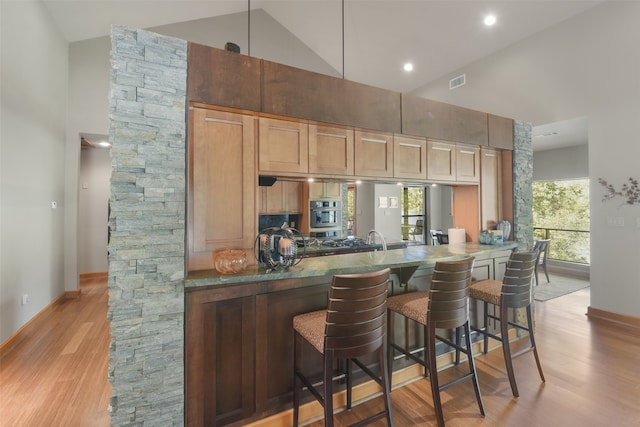 kitchen featuring kitchen peninsula, a kitchen bar, light wood-type flooring, and high vaulted ceiling