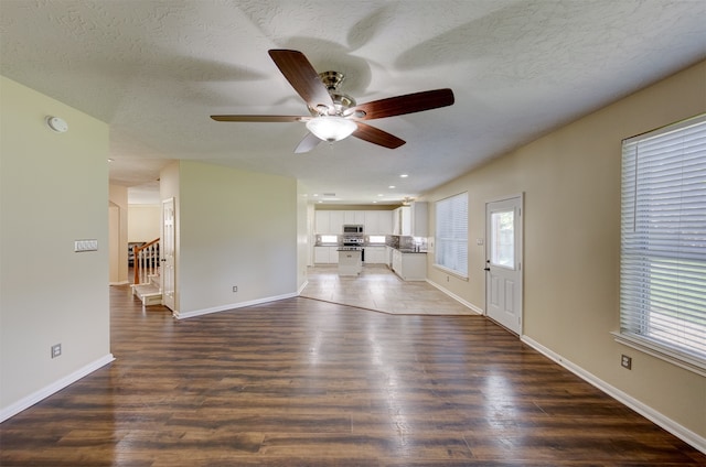 unfurnished living room featuring ceiling fan, a textured ceiling, and dark hardwood / wood-style flooring