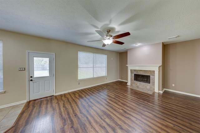 unfurnished living room featuring dark wood-type flooring, a tiled fireplace, a textured ceiling, and ceiling fan