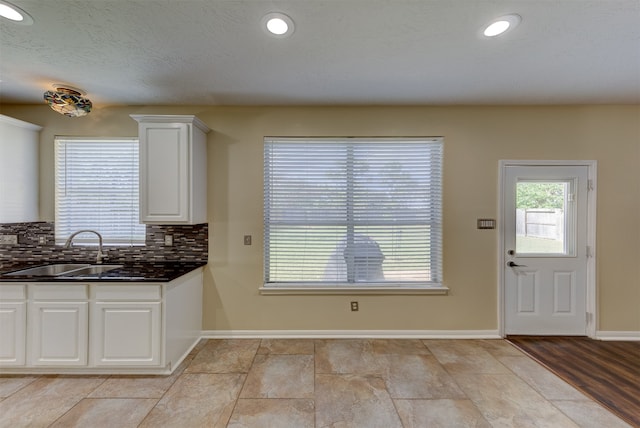 kitchen featuring sink, light wood-type flooring, backsplash, a textured ceiling, and white cabinetry