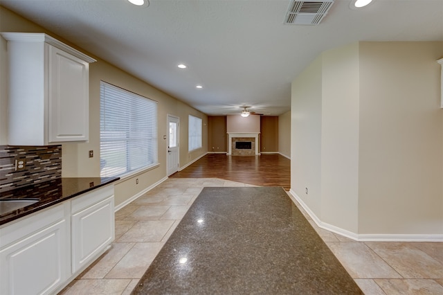 interior space with decorative backsplash, white cabinets, dark stone countertops, and ceiling fan