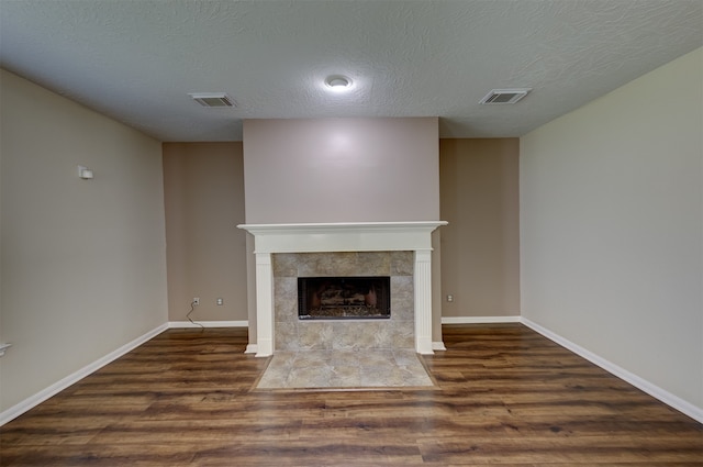 unfurnished living room featuring a textured ceiling, dark wood-type flooring, and a tile fireplace