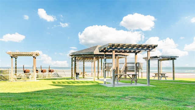 exterior space featuring a beach view, a lawn, a water view, and a pergola