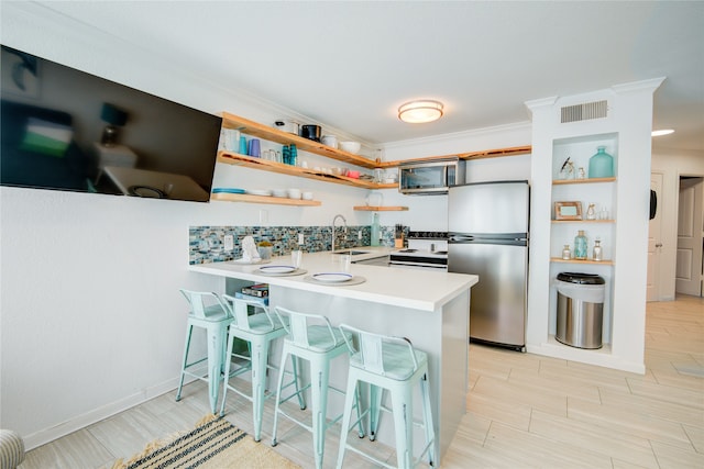 kitchen featuring kitchen peninsula, ornamental molding, stainless steel appliances, and a breakfast bar