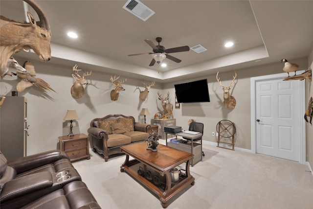 living room with ceiling fan, light colored carpet, and a raised ceiling