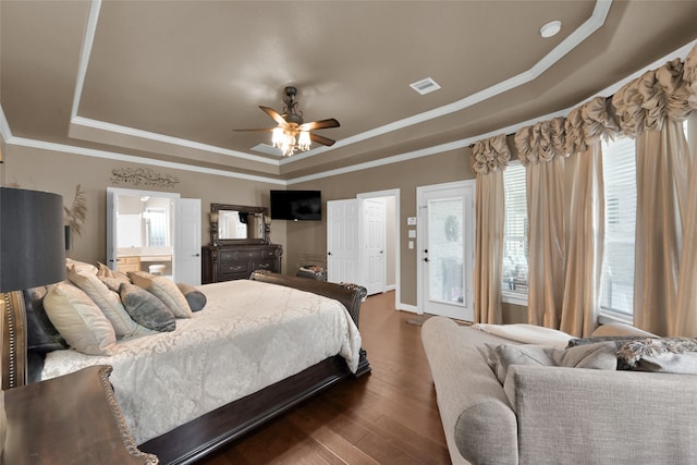 bedroom featuring ceiling fan, dark hardwood / wood-style flooring, a tray ceiling, ensuite bathroom, and crown molding