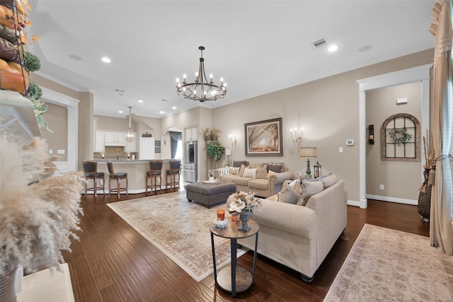 living room with dark wood-type flooring, crown molding, and an inviting chandelier