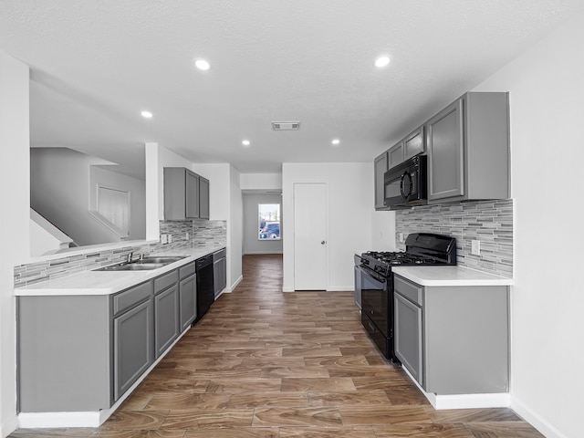 kitchen with sink, black appliances, dark wood-type flooring, and gray cabinetry