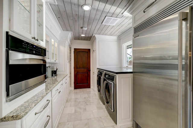 kitchen with appliances with stainless steel finishes, white cabinetry, light stone countertops, and separate washer and dryer