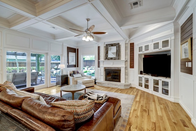 living room featuring coffered ceiling, beamed ceiling, ornamental molding, light wood-type flooring, and a fireplace