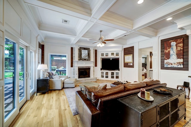 living room featuring beam ceiling, light hardwood / wood-style flooring, a fireplace, crown molding, and coffered ceiling