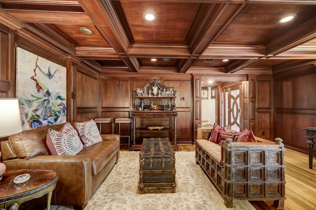 living room featuring coffered ceiling, ornamental molding, light hardwood / wood-style flooring, and wood walls