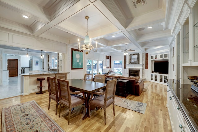 dining space featuring light hardwood / wood-style floors, coffered ceiling, beamed ceiling, and a large fireplace